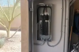 Open electrical service panel with EV breaker and conduit near a garage door in Phoenix, AZ.