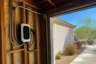 Wall-mounted EV charger and exposed timber studs with a view of desert landscaping in a Phoenix, AZ garage.