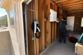 Technician cleaning a wall-mounted EV charger installed on timber studs in a Phoenix, AZ garage.