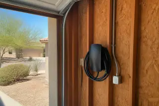 Wall-mounted EV charger with conduit and visible wiring on timber studs in a Phoenix, AZ garage.