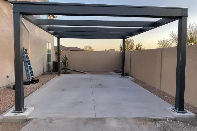 Metal carport skeleton installed over a paved parking space in Mesa, AZ, with gravel ground and stucco wall.