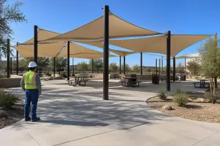Technician observing a tensioned membrane shade array over a public plaza in Gilbert, AZ.