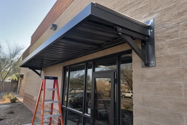 Metal awning installation above a commercial brick storefront in Scottsdale, AZ.