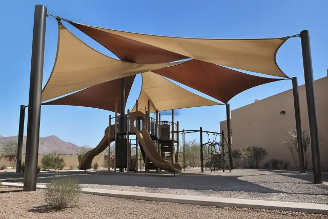 Multi-sail curved hip shade structure installed over a playground in Apache Junction, AZ.
