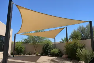 Triangular fabric shade sail tensioned between steel posts over a courtyard in Gilbert, AZ.