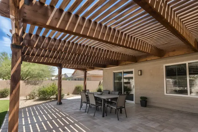 Sunlight filtering through a slatted pergola roof onto a travertine paver deck in Gilbert, AZ.