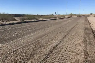 Coarse textured asphalt base layer exposed after milling, surrounded by desert creosote bushes in Goodyear, AZ.