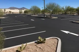 Freshly paved asphalt parking lot with white stall markings and prickly pear cactus landscaping in Goodyear, AZ.