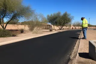 Worker in high-visibility gear inspecting a freshly paved asphalt surface in Goodyear, AZ.