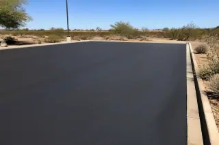 Freshly paved dark asphalt surface with desert scrub under bright sunlight in Goodyear, AZ.