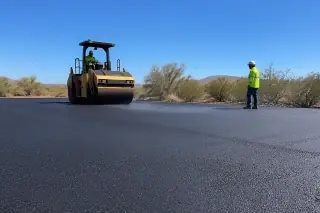 Vibratory roller compacting hot asphalt on a jobsite with desert vegetation in Goodyear, AZ.