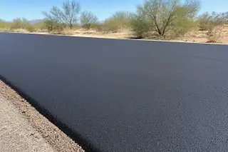 Finished dark asphalt surface with desert creosote bushes under bright sunlight in Goodyear, AZ.