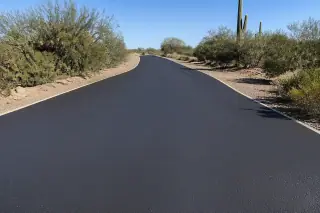 Newly sealed dark asphalt parking surface framed by desert creosote bushes in Goodyear, AZ.