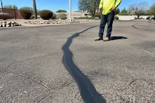 Rubberized sealant filling a linear crack in an asphalt surface with desert xeriscaping in Goodyear, AZ.