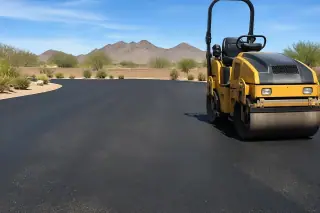 Vibratory roller smoothing dark asphalt with a desert mountain backdrop in Goodyear, AZ.