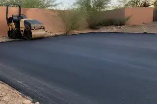 Vibratory roller parked on a newly paved asphalt surface near desert creosote bushes in Goodyear, AZ.
