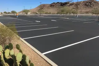 Contractor inspecting white parking stall lines on new asphalt with prickly pear cactus in Goodyear, AZ.