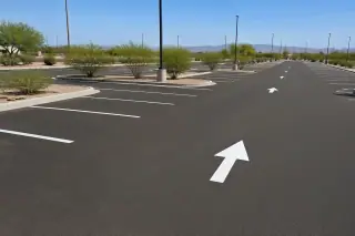 Parking lot grid layout with white stall lines and directional arrows near desert creosote bushes in Goodyear, AZ.