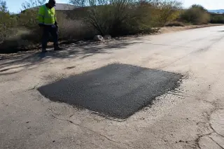 Contractor inspecting a freshly compacted asphalt pothole repair in Goodyear, AZ.