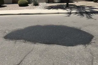 Freshly compacted asphalt patch repairing a pothole in an aged road in Goodyear, AZ.