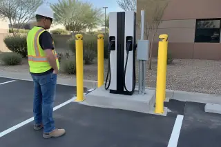 Technician observing a new commercial EV charger on a concrete island in Mesa, AZ.