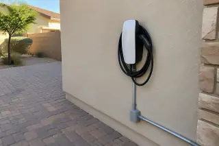 Wall connector mounted on an exterior house wall next to a paved brick driveway in Mesa, AZ.