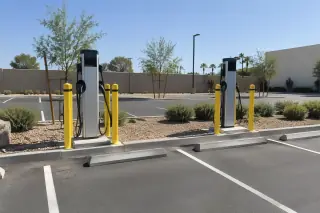 Dual pedestal EV charging stations and concrete wheel stops in a paved employee parking lot in Mesa, AZ.
