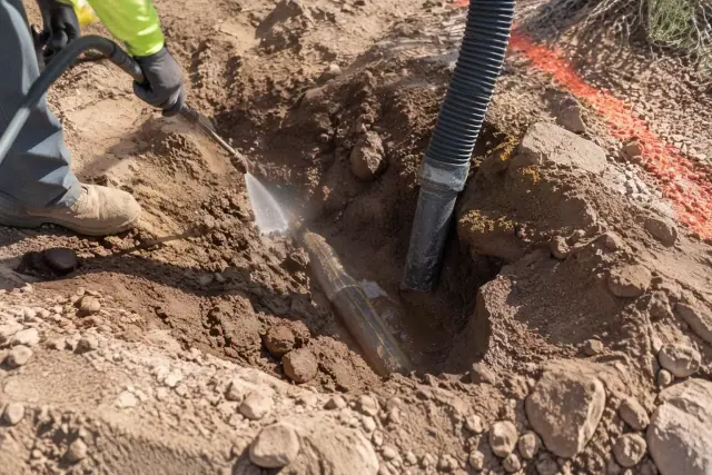 Contractor hand exposing a buried utility line in damp desert soil in Mesa, AZ.