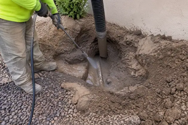 Muddy soil slurry pooled around an uncovered utility line in a yard in Mesa, AZ.