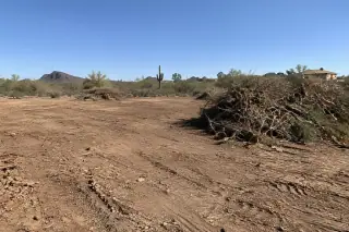 Completed land clearing project detail showing cleared earth and stacked debris in Mesa, AZ.