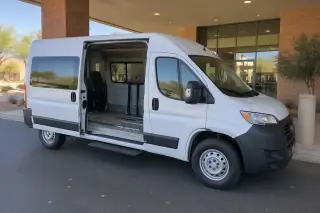 White transport van parked under a covered brick drop-off lane in Mesa, AZ.