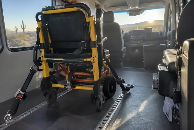 Stair chair transportation secured in a vehicle in Mesa, AZ, with desert sun glare and floor dust.
