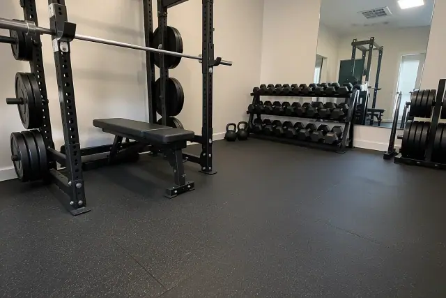 Rubber flooring installed under barbell racks and dumbbell storage in a Gilbert, AZ indoor gym.