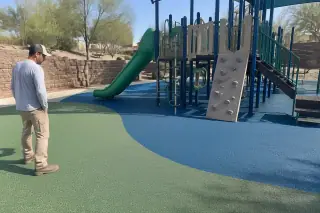 Contractor inspecting seamless rubber safety surfacing near a climbing set in Mesa, AZ.