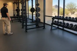 Service professional inspecting rolled rubber flooring and barbell racks in Mesa, AZ.