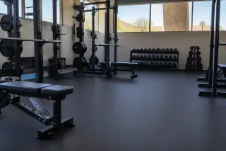 Wide view of thick rubber flooring installed under barbell racks and dumbbell stations in Mesa, AZ.