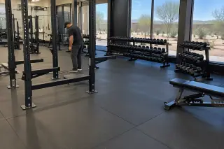 Service professional inspecting rubber flooring and barbell racks in Mesa, AZ.