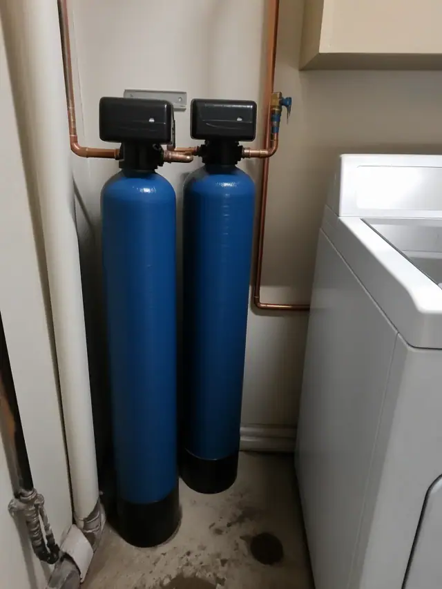 Whole house water filtration system with blue tanks and copper pipes in a laundry room in Glendale, AZ.