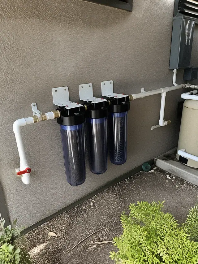 Carbon filtration system with PVC piping installed on an outdoor stucco wall in Mesa, AZ.