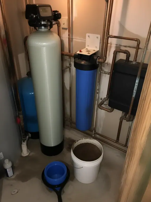 A water filtration system with copper pipes and a filter media bucket in a mechanical room in Mesa, AZ.
