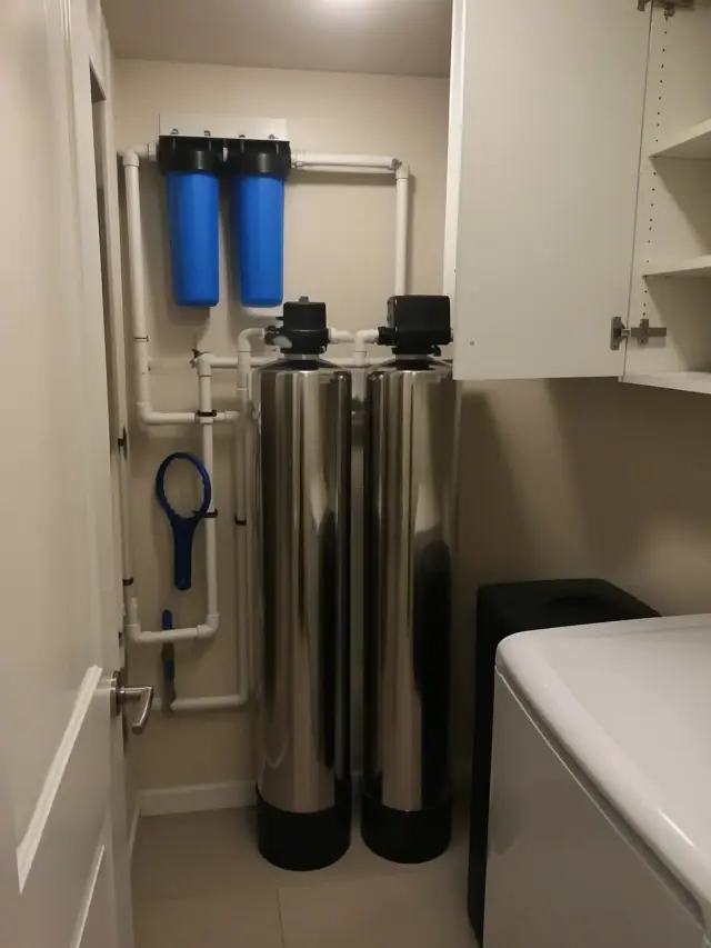 Newly installed water filtration system with stainless steel tanks and white piping in a Scottsdale, AZ laundry room.