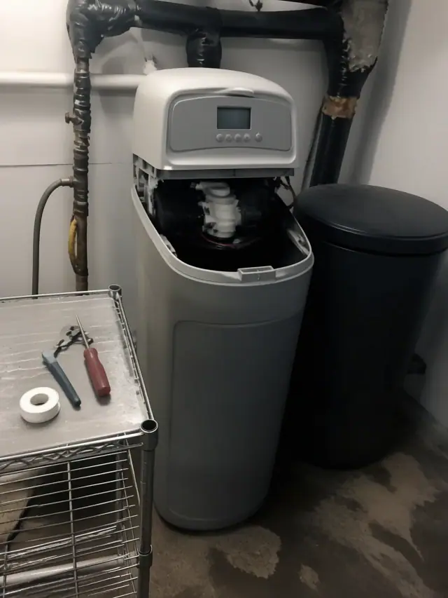 Repaired water softener in an office utility closet in Mesa, AZ, with tools on a shelf.