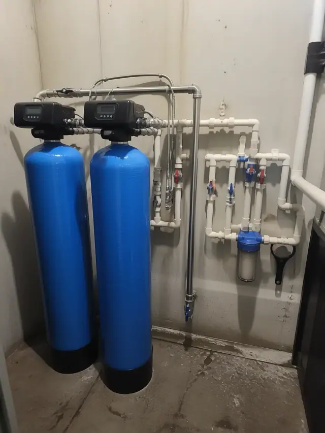 Commercial water softener system with blue tanks and stainless steel piping in a Tempe, AZ utility room.