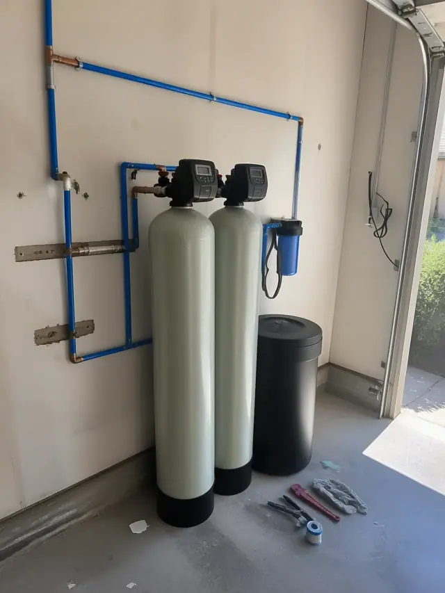 Newly installed water softener system with two resin tanks and blue piping in a residential garage in Glendale, AZ.