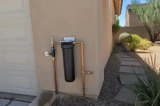 Finished carbon filtration system with piping and filter housings mounted on a stucco wall in Mesa, AZ.