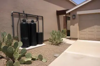 Carbon filtration system with industrial piping installed on a stucco wall near prickly pear cacti in Mesa, AZ.