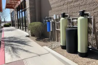 Commercial water softener tanks and plumbing installed outside a retail storefront in Mesa, AZ.