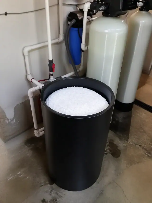 Commercial water filtration system with a brine tank and PVC piping in a utility room in Mesa, AZ.