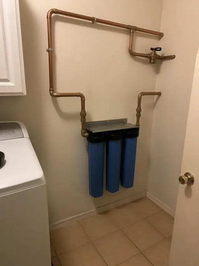 Newly installed water filtration system with blue canisters and copper pipes in a Gilbert, AZ laundry room.
