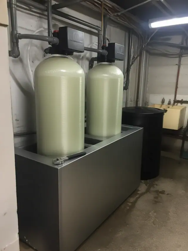 Two industrial water softener tanks with new tubing and a wrench in a utility room in Mesa, AZ.